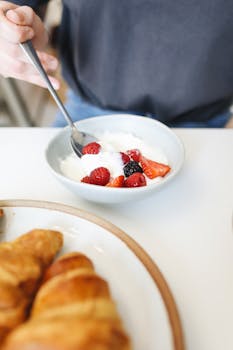 A delicious plate of yogurt topped with fresh berries beside golden croissants, perfect for a nutritious breakfast.