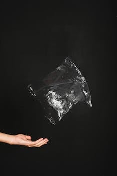 A hand tosses a plastic bag against a black background, illustrating environmental concerns.