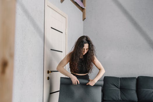 A woman sets up an exercise mat in a modern, minimalist apartment living room.