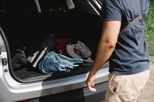 Man organizing camping gear in car trunk, ready for adventure.