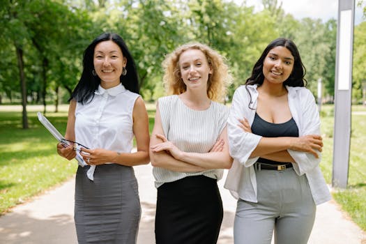 Three smiling businesswomen standing arm in arm in a sunny park, exuding confidence and camaraderie.