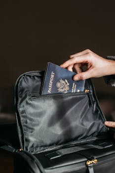 Close-up of a person placing a passport into a leather bag, ready for travel.