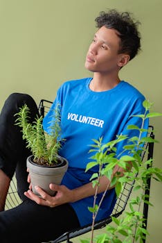 Portrait of a young volunteer in blue shirt sitting with a potted plant against a green background.