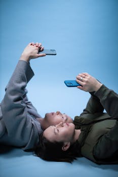 Two adults lying down, using smartphones against a bright blue backdrop.