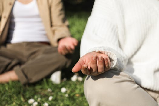 Two people meditating outdoors, focusing on hands in a peaceful setting.