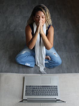 A woman practicing meditation in front of a laptop to promote mindfulness and mental wellness.